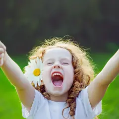 Szczęśliwa dziewczynka z rumiankiem we włosach pokazuje kciuki w górę.